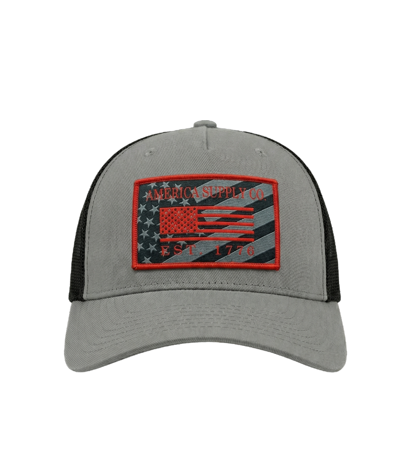 The Alex Jones Store - Front view of grey America Supply Co patch trucker hat with red-bordered American flag Est. 1776 woven patch