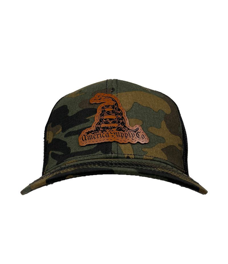 The Alex Jones Store - Front view of camo America Supply Co Gadsden leather patch trucker hat with coiled rattlesnake design on black mesh