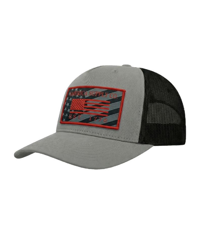 The Alex Jones Store - Angled side view of grey America Supply Co trucker hat with red-bordered American flag patch and black mesh back