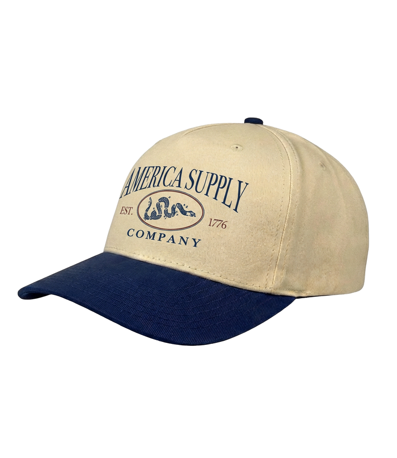The Alex Jones Store - Tan and navy America Supply Co. 'Est. 1776' Trucker Hat with rattlesnake oval logo, side-angle showing curved navy bill