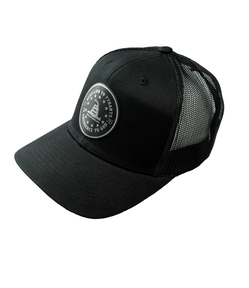 The Alex Jones Store - Three-quarter view of black trucker hat with Obedience To God circle star leather patch and mesh back
