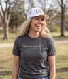 The Alex Jones Store - Blonde woman laughing outdoors in gray America Supply Co. 'Est. 1776' tee and white USA trucker hat