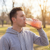 Alex Jones Naturals - Optimal Human Hydration Drink Mix with French Sea Salt — Man in gray hoodie drinking pink Optimal Human strawberry lemonade hydration drink from OH glass bottle outdoors at sunset